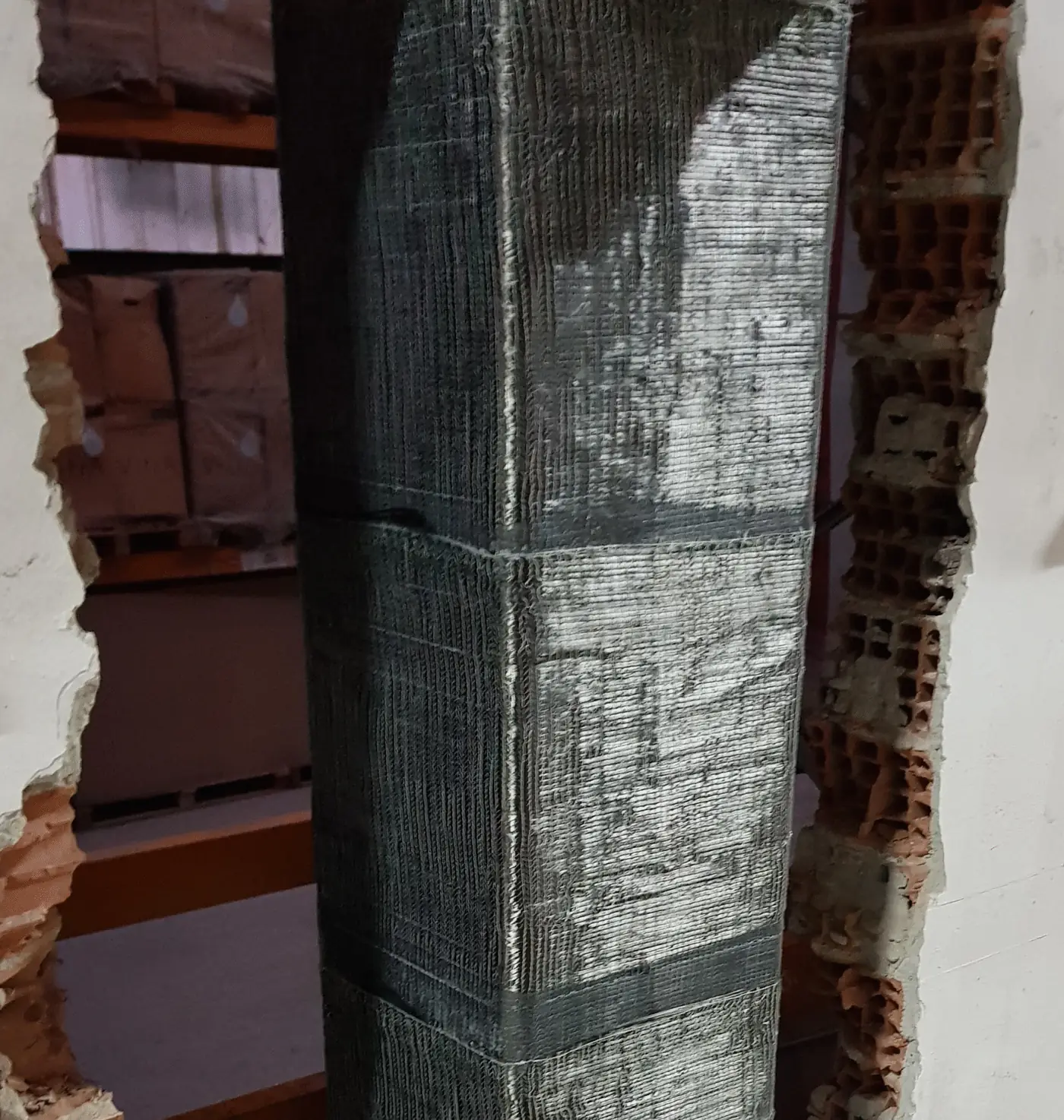 Tuğla dolgu duvarı açılmış bir yerde, dört yüzü karbon lifli kumaşla sarılmış kolon; kumaş katları yatay ve üst üste binmiş.